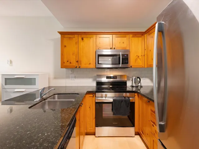 Kitchen featuring appliances with stainless steel finishes, dark stone counters, backsplash, and brown cabinetry