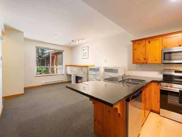 Kitchen with tasteful backsplash, appliances with stainless steel finishes, brown cabinetry, and a lit fireplace