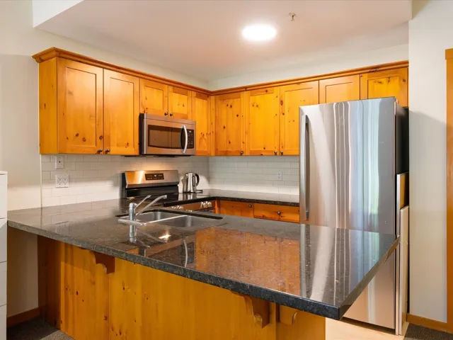 Kitchen with a peninsula, dark stone countertops, stainless steel appliances, and backsplash