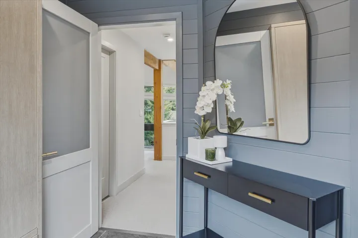 Hallway featuring blue horizontal plank wall paneling, a dark console table with gold-toned hardware, and a contemporary arched mirror
