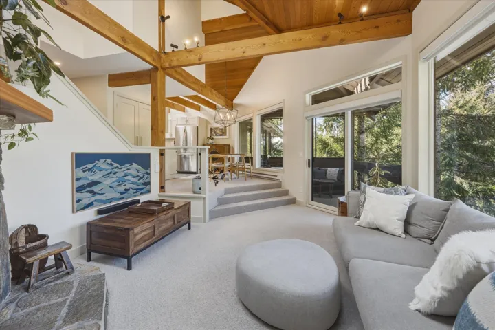Great room featuring exposed wood beams, wood ceiling, stone fireplace, and ample natural light from extensive glazing