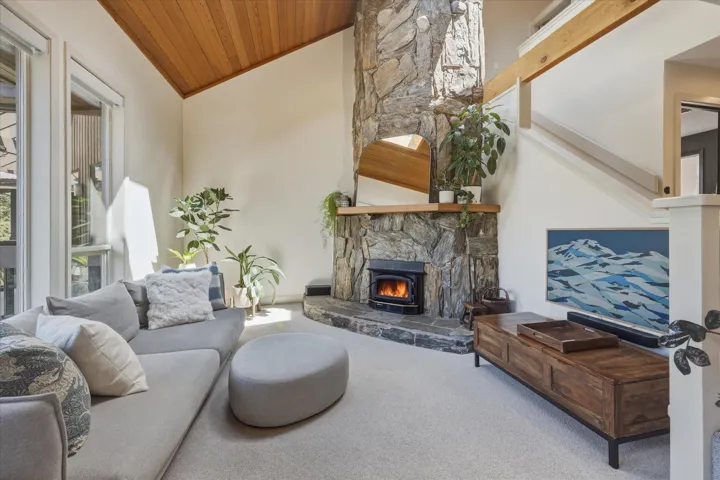 Living space featuring a stone fireplace with a wood-burning insert, vaulted wood-paneled ceiling, and large windows