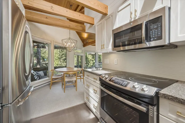 Kitchen featuring stainless steel appliances, white cabinetry with gold-tone hardware, a tiled backsplash, and stone countertops