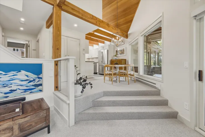 Split-level living area featuring exposed wood beams, a wood-paneled vaulted ceiling, and an open concept kitchen with stainless steel appliances