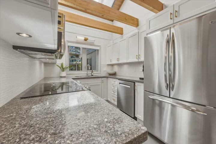 Kitchen featuring exposed wood beams, white cabinetry, stainless steel appliances, a built-in cooktop, and speckled countertops