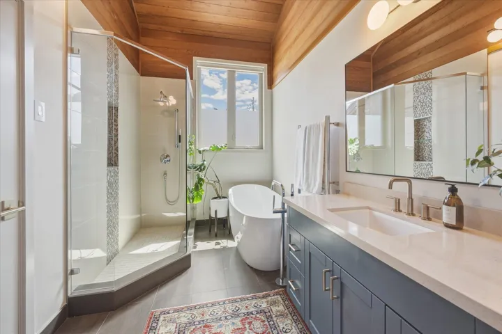Bathroom featuring a freestanding soaking tub, glass-enclosed shower with tiled accents, and a dual-sink vanity with a light-toned countertop