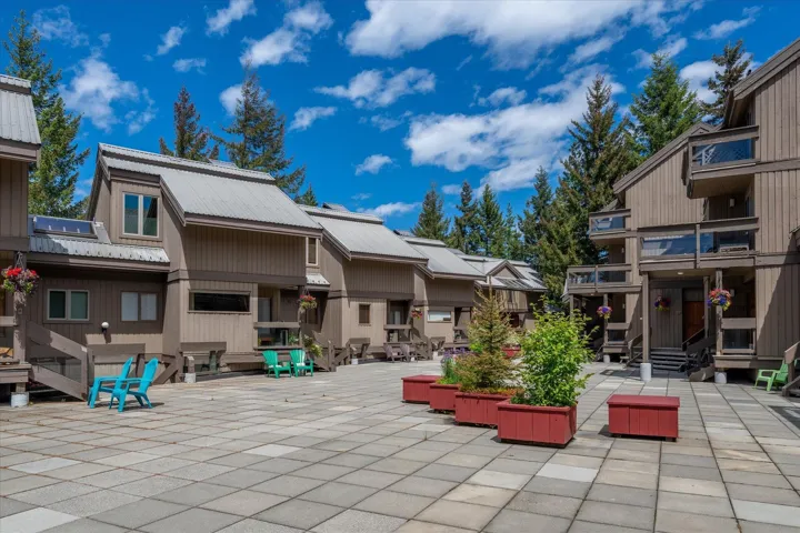 Modern townhomes featuring a central paved courtyard with planter boxes, private balconies, and surrounding mature evergreen trees