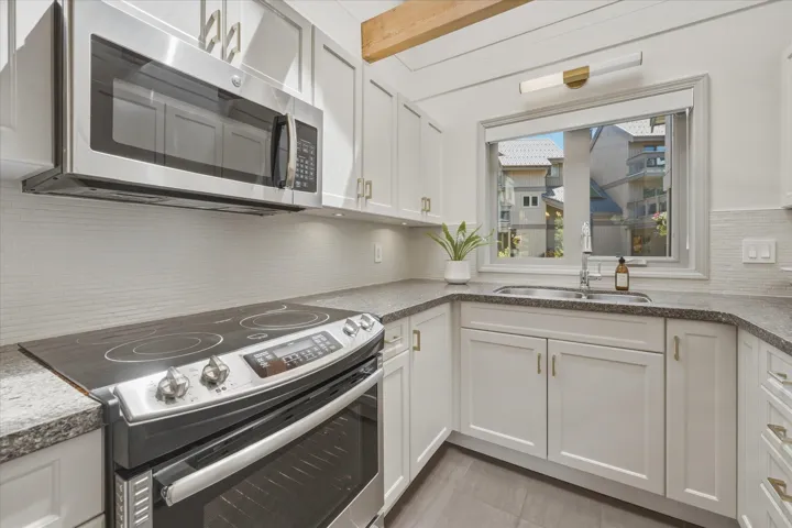 Kitchen featuring stainless steel appliances, white cabinetry with gold-tone hardware, granite countertops, and a full tile backsplash