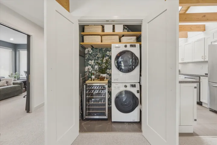 Dedicated laundry closet with stacked washer and dryer, integrated shelving, and patterned wallpaper