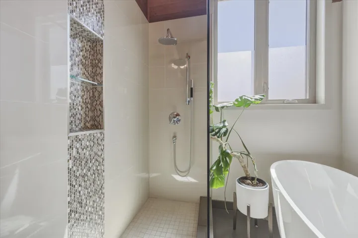 Tiled shower enclosure featuring a mosaic accent niche with glass shelving, an overhead showerhead, and a handheld shower fixture