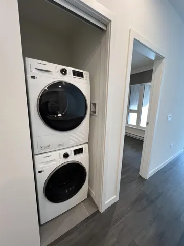 Laundry area with stacked washer / dryer, dark wood-type flooring, a baseboard heating unit, and crown molding