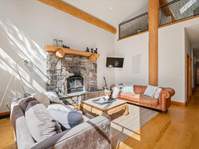 Living room featuring wood-type flooring, a fireplace, high vaulted ceiling, and beamed ceiling