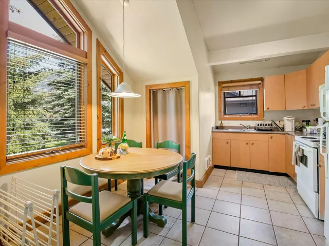 Kitchen with light tile patterned flooring, white stove, pendant lighting, light brown cabinetry, and dark countertops