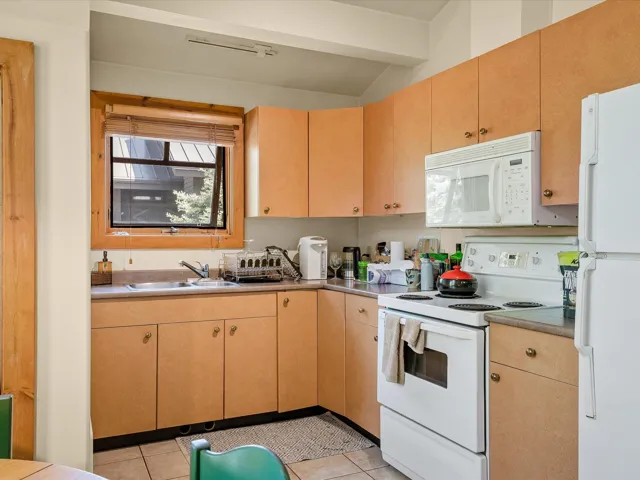 Kitchen featuring white appliances, light tile patterned floors, light countertops, beamed ceiling, and light brown cabinetry