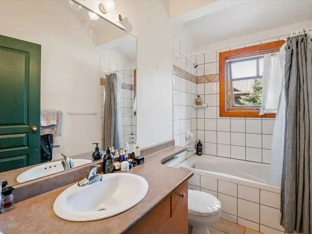 Bathroom with tiled shower / bath combo, vanity, vaulted ceiling, and light tile patterned floors