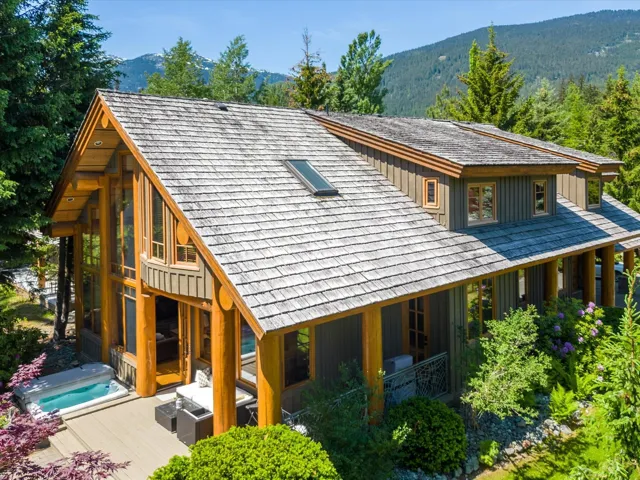 Back of property featuring a mountain view, an outdoor hot tub, and a wooded view