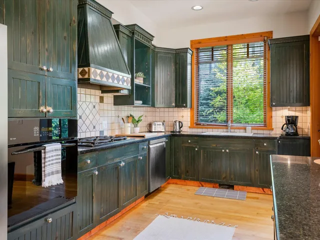 Kitchen featuring black appliances, custom exhaust hood, light wood finished floors, decorative backsplash, and glass insert cabinets