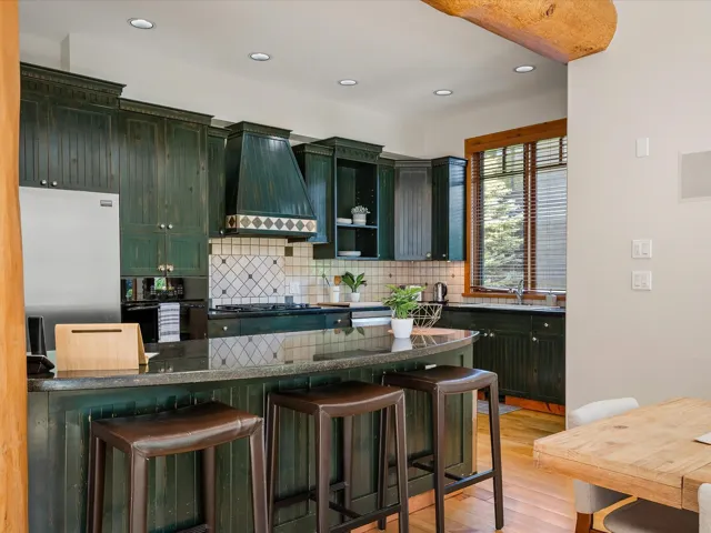 Kitchen with green cabinets, tasteful backsplash, a breakfast bar area, recessed lighting, and freestanding refrigerator