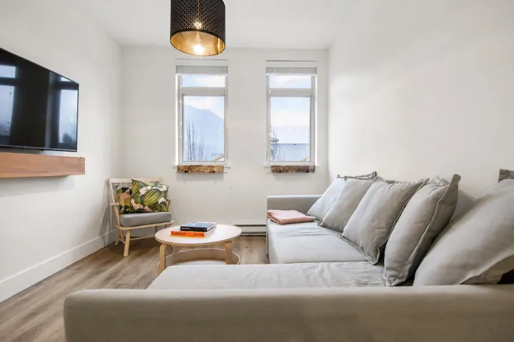 Living area featuring wood-finish flooring, two large windows, a floating wood shelf, and a ceiling-mounted light fixture