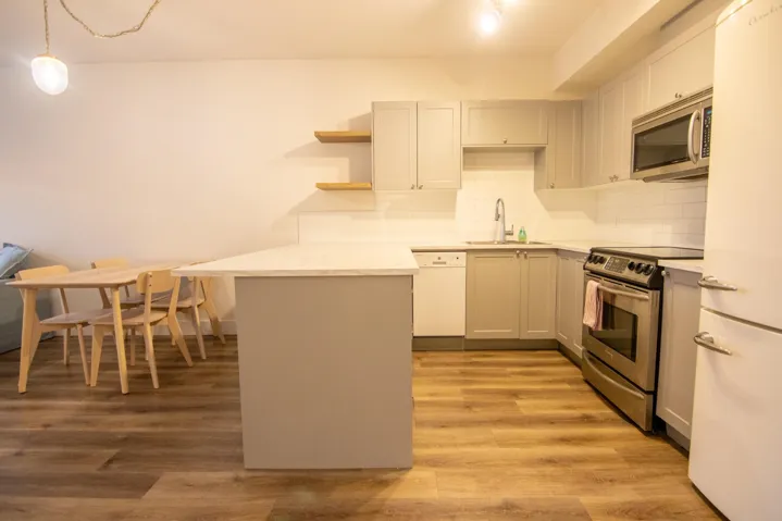 Kitchen featuring appliances with stainless steel finishes, a peninsula, light wood finished floors, tasteful backsplash, and hanging light fixtures