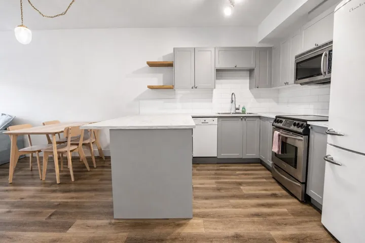Modern kitchen featuring light gray cabinetry, white subway tile backsplash, stainless steel appliances, a white countertop, and wood-finish flooring