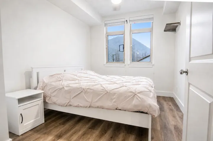 Bedroom featuring wood-finish flooring, white baseboards, and two windows showcasing a prominent mountain backdrop