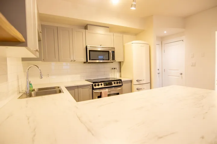 Kitchen with stainless steel appliances, light stone counters, decorative backsplash, and gray cabinetry