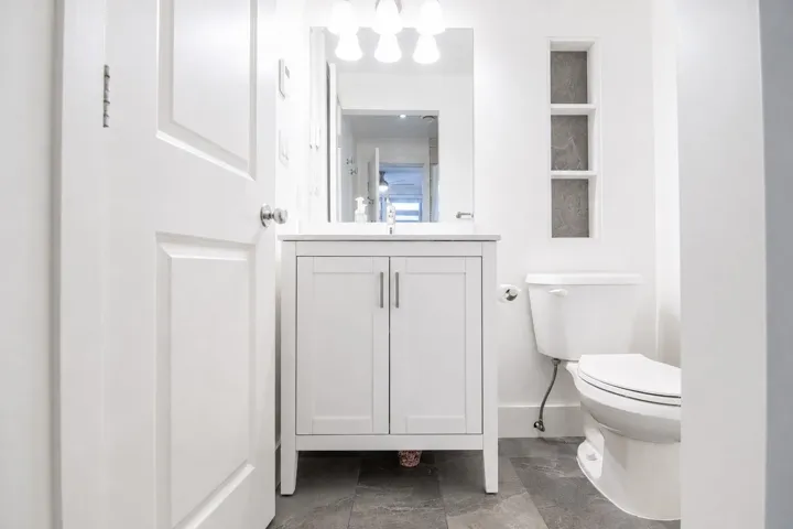 Bathroom featuring a white vanity with brushed nickel hardware, a rectangular mirror, and a three-bulb light fixture