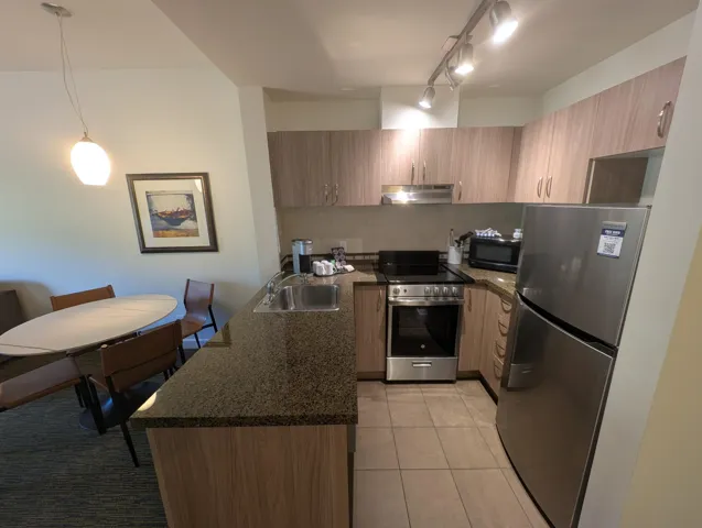Kitchen with stainless steel appliances, dark stone counters, light tile patterned flooring, a peninsula, and rail lighting