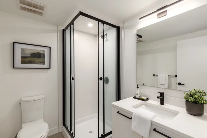 Modern bathroom featuring a glass-enclosed shower with black framing, a white vanity with a rectangular undermount sink, a stone countertop, and matte black fixtures