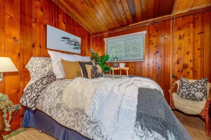Wood-paneled room featuring an angled ceiling, horizontal window with blinds, and a built-in wall sconce