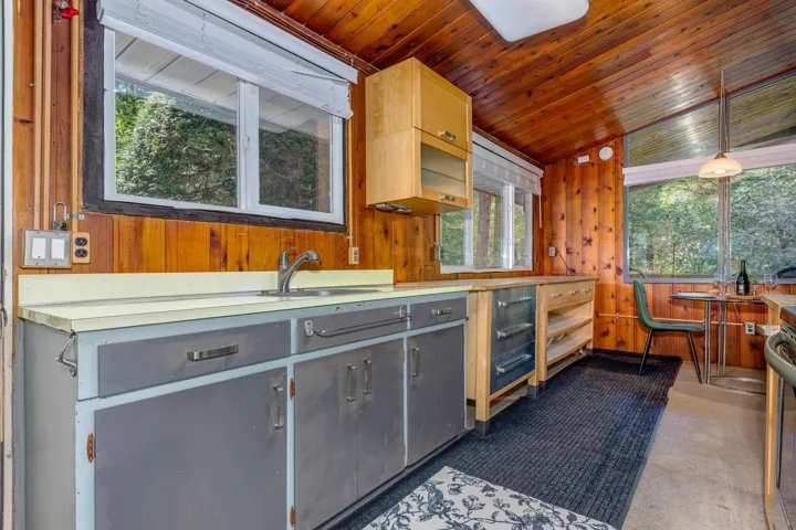Kitchen space featuring wood paneling, a stainless steel sink, and exposed cabinetry with gray and wood-finish doors