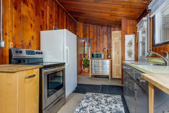 Wood-paneled kitchen featuring stainless steel range, white refrigerator, light wood-finish cabinetry, and a countertop with an undermount sink