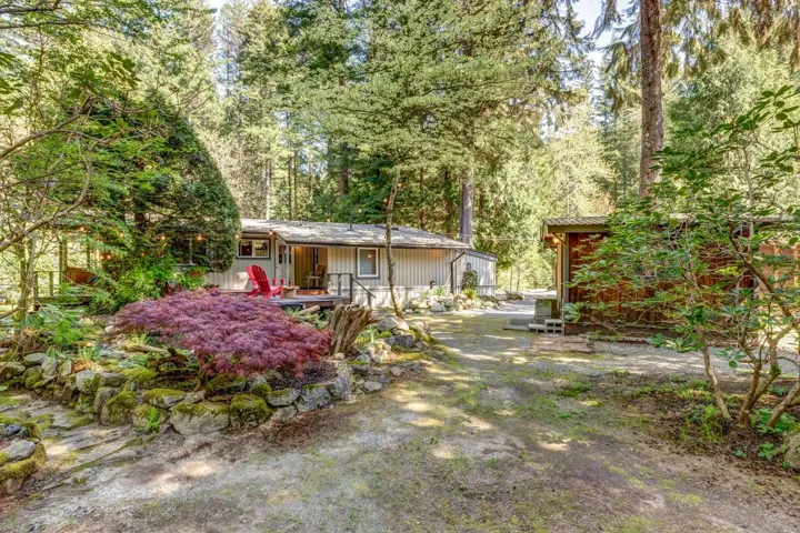 Wooded property featuring a main residence with a covered porch, an additional detached structure, and a natural rock retaining wall