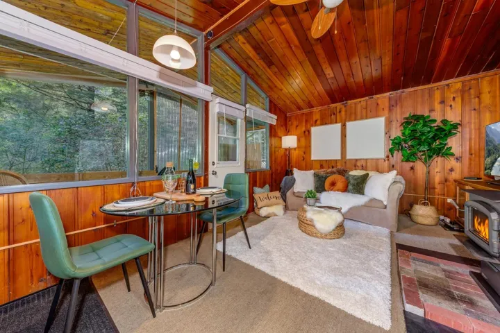 Vaulted wood-paneled ceiling with a ceiling fan, wood-paneled walls, and a freestanding wood-burning stove with a brick hearth