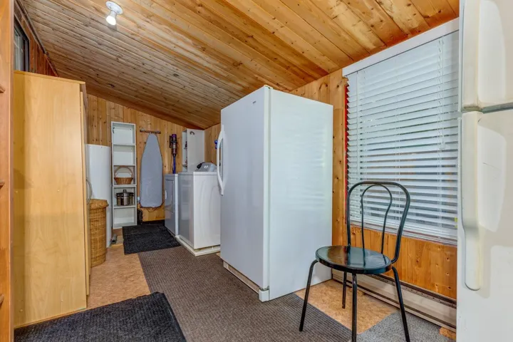 Utility space featuring paneled wood walls and ceiling, a window with blinds, and durable flooring