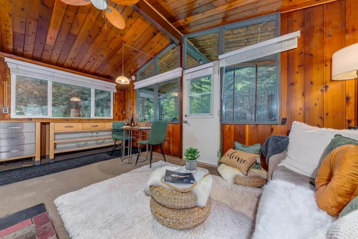 Vaulted wood-paneled ceilings with exposed beams, wood-paneled walls, large windows offering natural light, built-in shelving, and a prominent ceiling fan