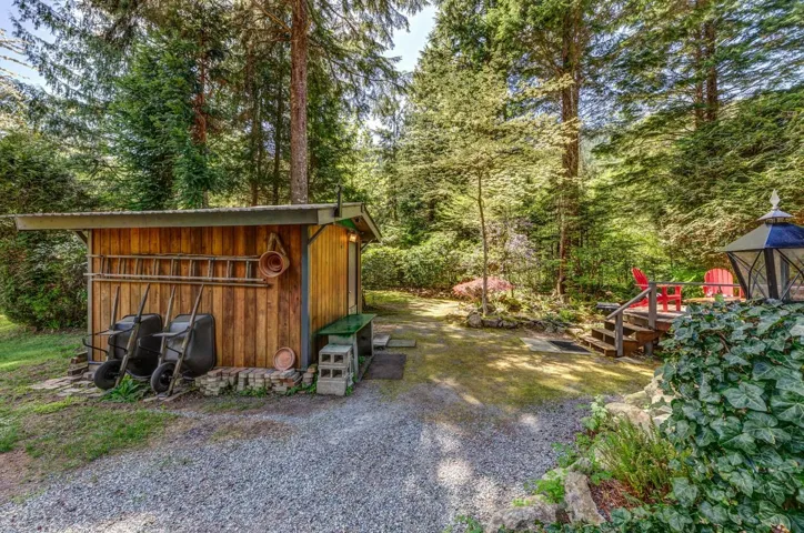 Wood-sided outbuilding with a metal roof, gravel driveway, wood deck, and lush natural landscaping