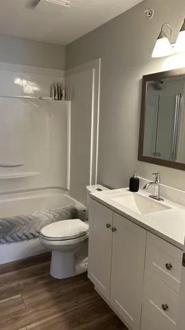 Bathroom featuring wood-finish flooring, a white vanity with an integrated sink, a chrome faucet, and a shower/tub combination