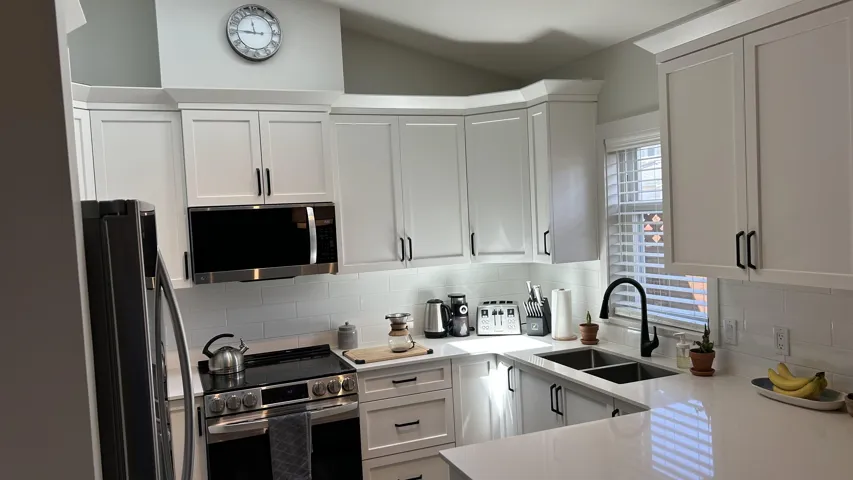 Modern kitchen featuring white shaker cabinetry, stainless steel appliances, a subway tile backsplash, quartz countertops, and a black gooseneck faucet