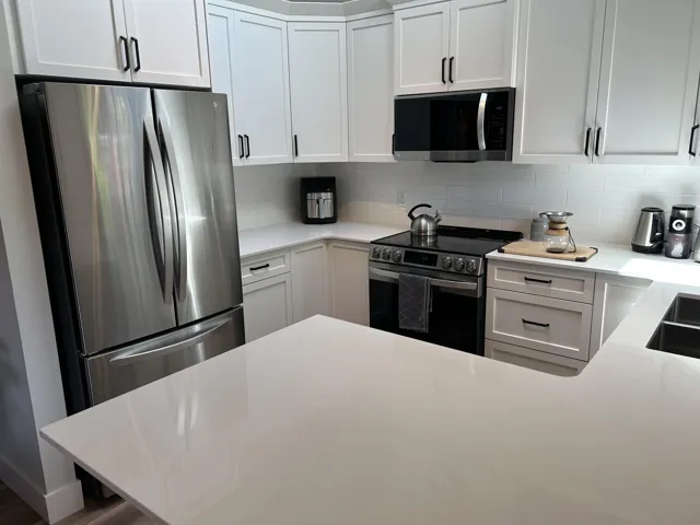 Modern kitchen featuring white shaker cabinetry with matte black hardware, white subway tile backsplash, and light-toned countertops