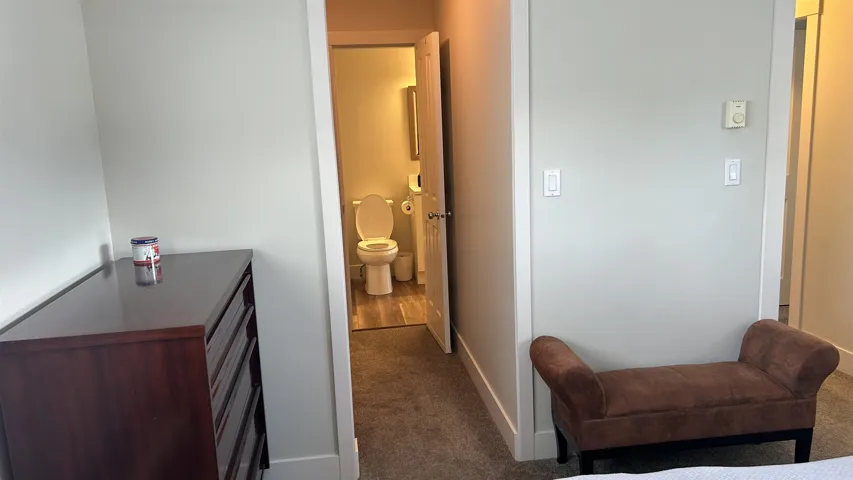 Bathroom featuring wood-finish flooring, a white toilet, and a wall-mounted mirror