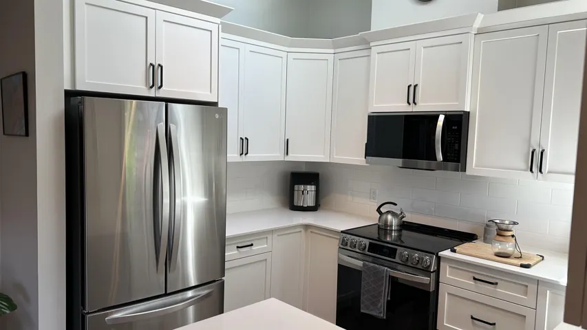 Modern kitchen featuring white cabinetry with black hardware, stainless steel appliances, white subway tile backsplash, and light-toned countertops