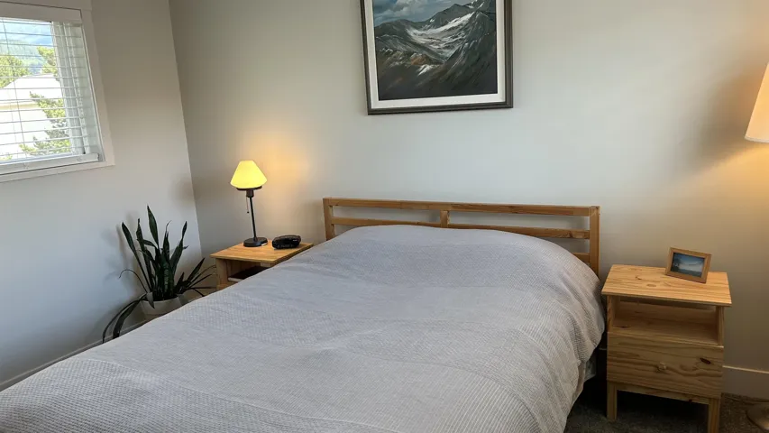Bedroom featuring light gray walls, wood-finish flooring, a window with horizontal blinds, and a built-in wooden headboard