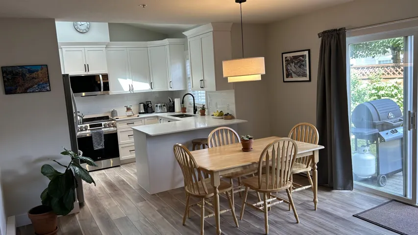 Open-concept kitchen and dining area featuring white shaker cabinetry, stainless steel appliances, a white tile backsplash, a kitchen island with seating, and wood-finish flooring