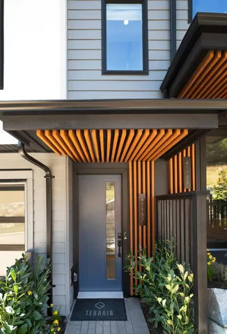 Contemporary entry featuring a blue door with vertical window panel, wood slat accents, black trim, and address numbers
