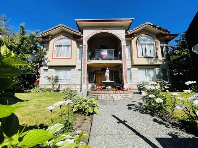 Stucco and brick facade with arched architectural elements, a second-story balcony, a prominent water feature, and a paved walkway leading to the entrance
