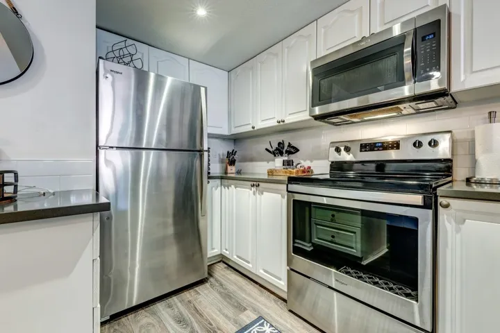 Kitchen with stainless steel appliances, dark countertops, white cabinetry, and light wood finished floors