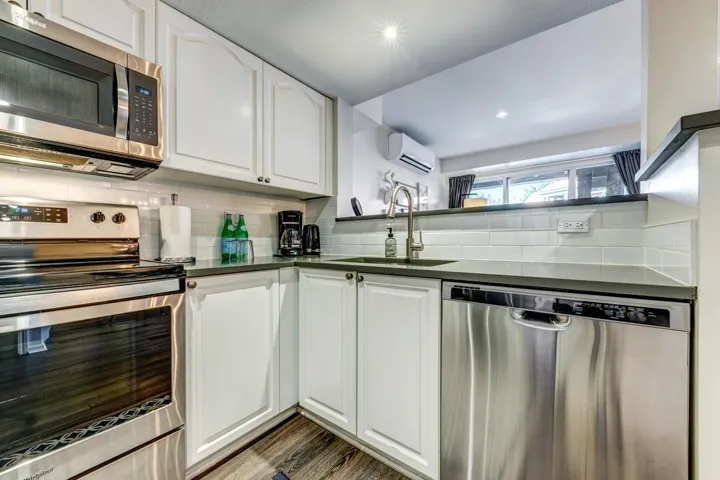 Kitchen featuring stainless steel appliances, dark countertops, decorative backsplash, white cabinets, and a sink