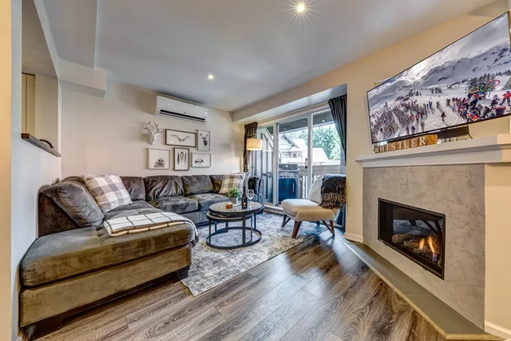 Living room with a wall unit AC, wood finished floors, and a glass covered fireplace